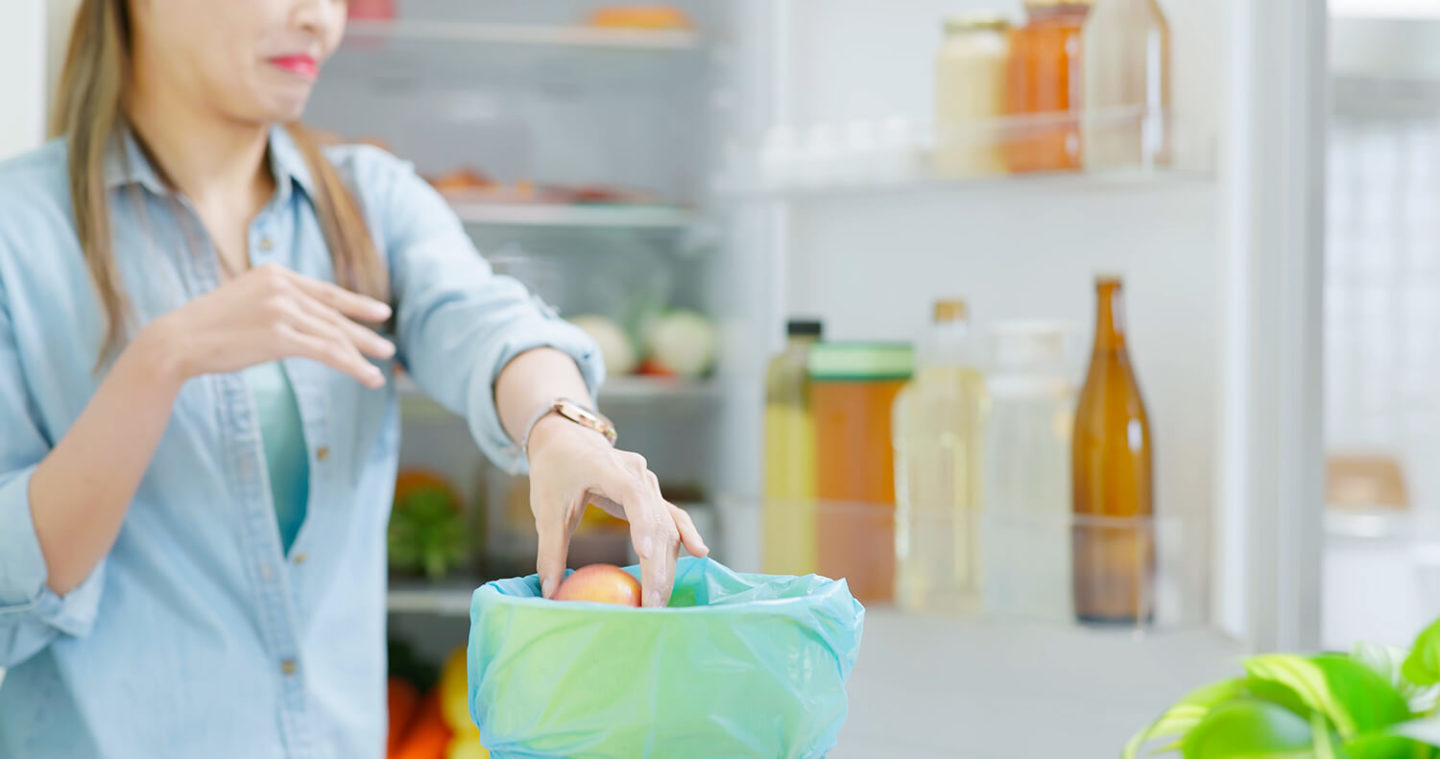 Людина прибирає з відкритої людини зіпсовані продукти і викидає їх у відро для сміття.